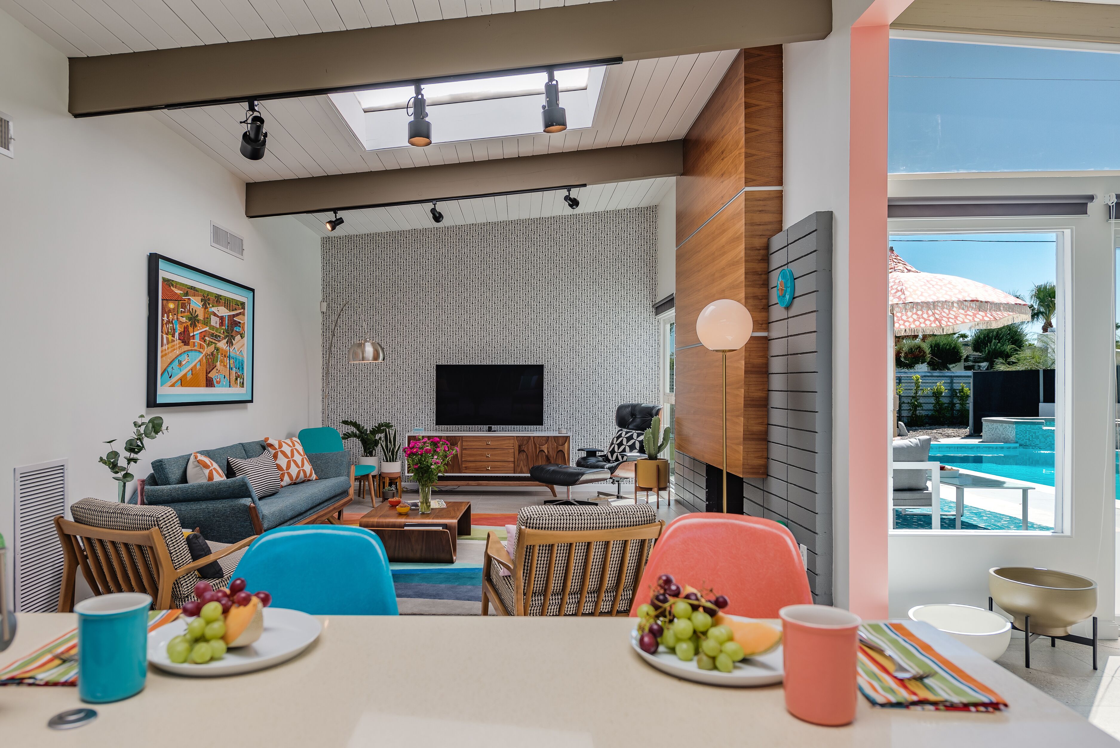 Una sala de estar moderna con un televisor de pantalla plana, un comedor con mesa dispuesta para dos personas y vistas a una piscina exterior.