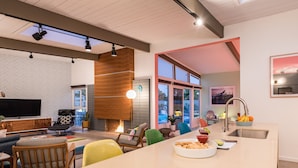 Una sala de estar moderna con chimenea, asientos cómodos, un televisor grande y una cocina con un lavabo y frutero.