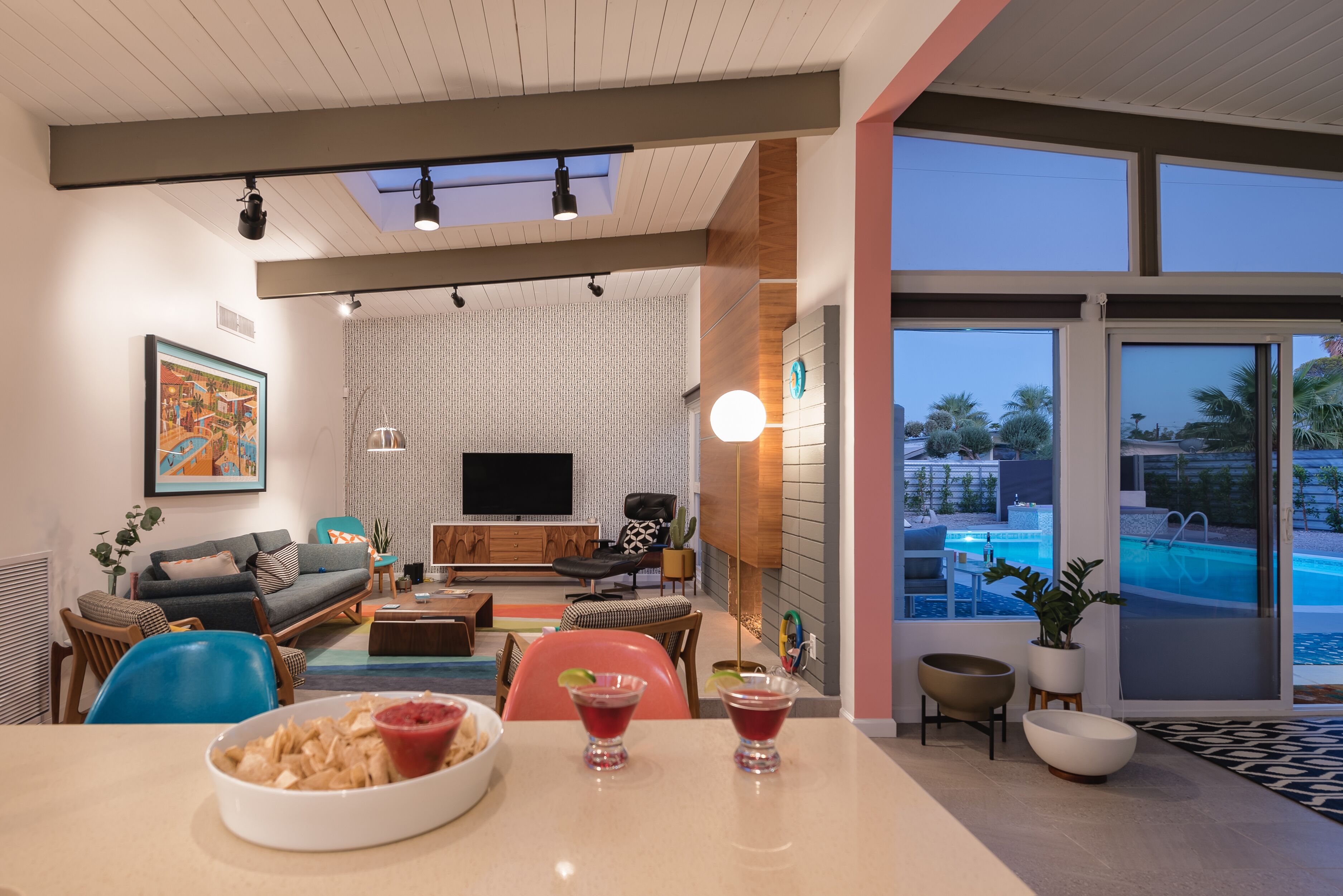 A modern living room with a large TV, comfortable seating, and a view of a swimming pool.