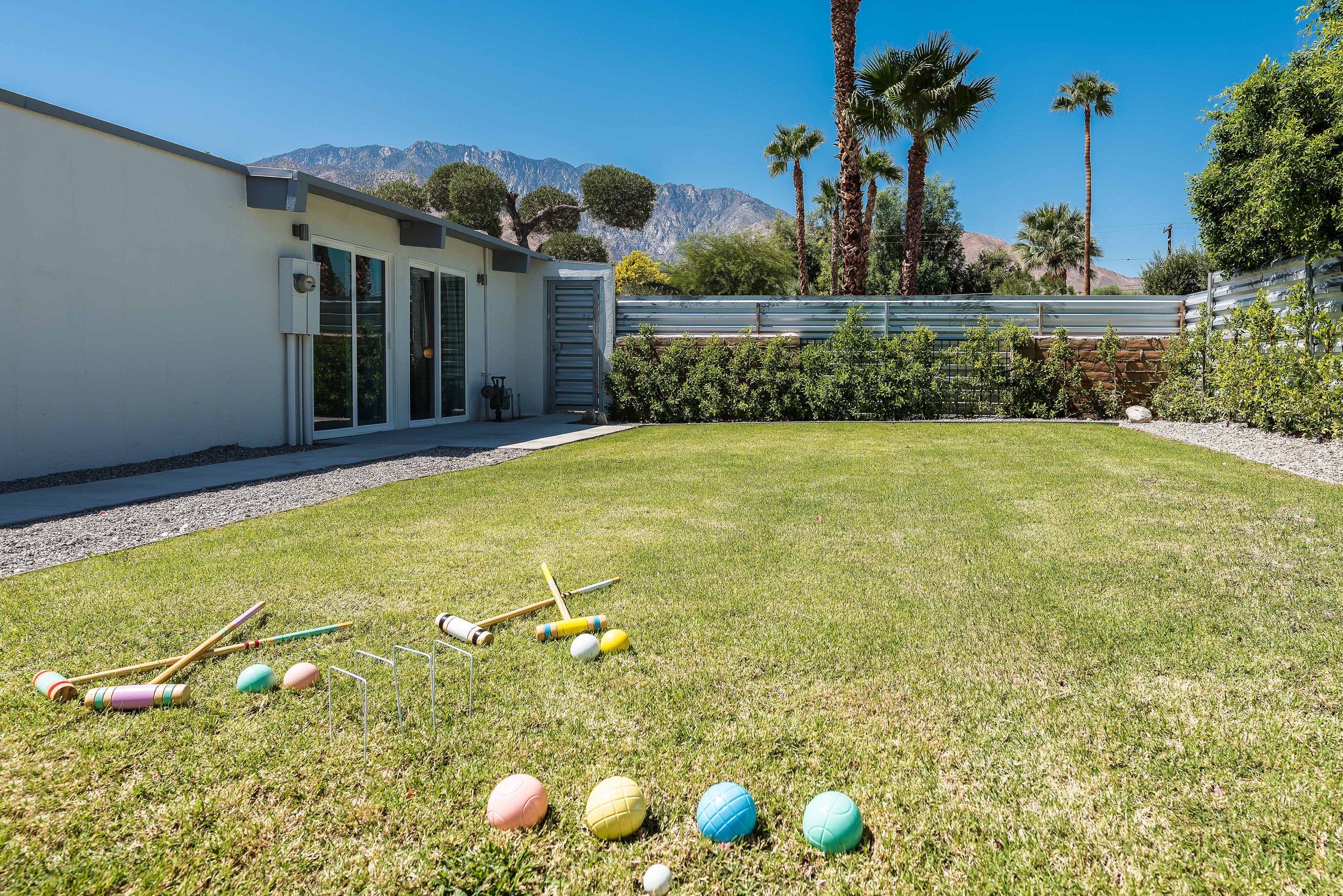 Une pelouse bien entretenue avec des équipements et des balles de croquet, un bâtiment moderne doté de grandes fenêtres et une chaîne de montagnes en arrière-plan.