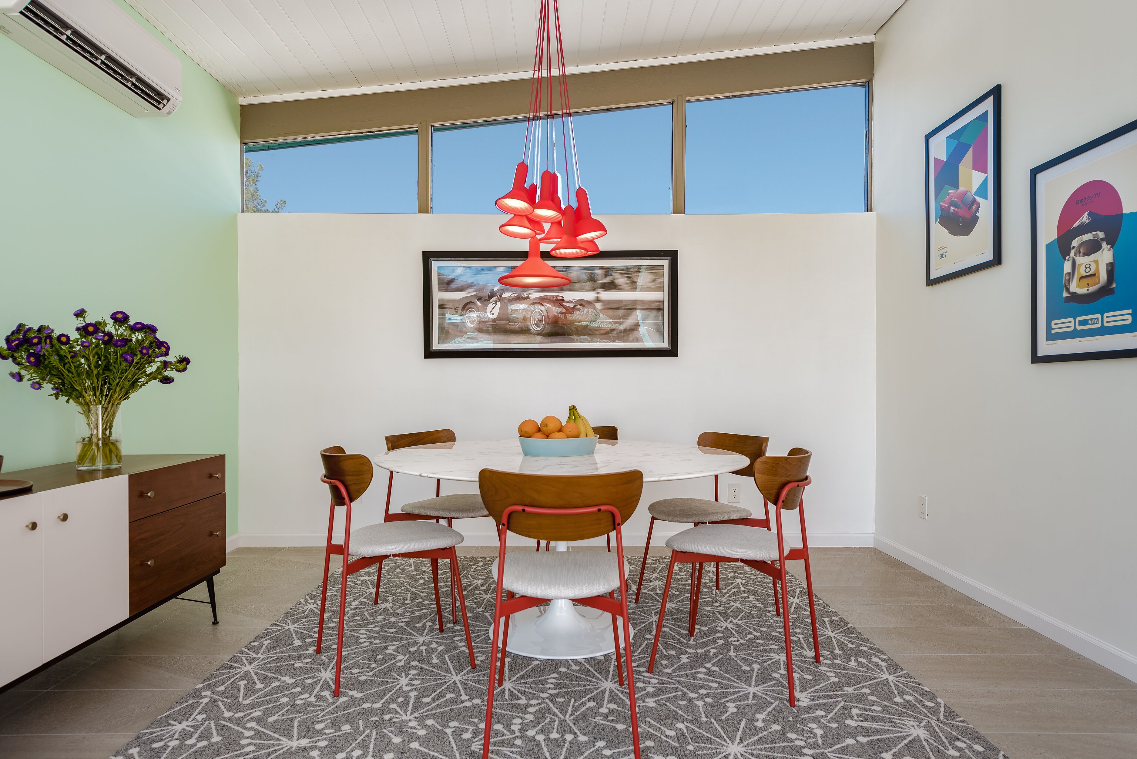 A dining area with a round table, six chairs, a vase of flowers, and a framed picture on the wall.