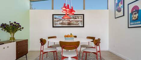 A dining area with a round table, six chairs, a vase of flowers, and a framed picture on the wall.