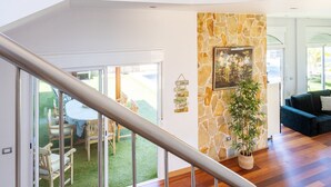 A spacious living area with a wooden staircase, a chandelier, a stone accent wall, and a dining area with outdoor access. - Villa Syrah Tenerife (Puerto De La Cruz)