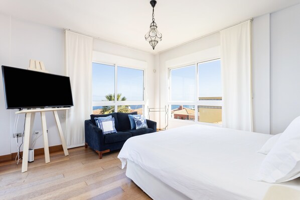 Habitación de hotel con una cama grande, televisor en un mueble bajo, sofá y balcón con vistas.
