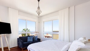 A bedroom with a bed, a TV, a sofa, and large windows with a view of the sea. - Villa Syrah Tenerife (Puerto De La Cruz)