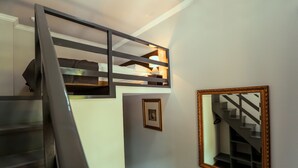A staircase with a metal railing leading to a lofted sleeping area. A framed mirror hangs on the wall. - Tea for Two Hotel (Tbilisi)