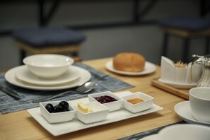 A breakfast setting with a plate of toast, a bowl of blackberries, a bowl of butter, a bowl of jam, and a cup of tea on a wooden table. - Tea for Two Hotel (Tbilisi)