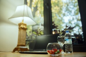 A laptop on a wooden table with a glass containing a red drink, a water bottle, and a lamp in the background. - Tea for Two Hotel (Tbilisi)