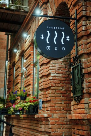 A round sign with numbers and symbols, mounted on a brick wall with windows and flower boxes. - Tea for Two Hotel (Tbilisi)