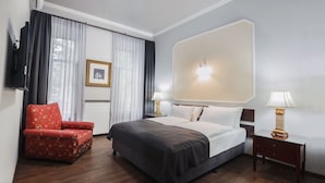 A hotel room with a bed, a red armchair, a nightstand with lamps, and a large mirror on the wall. - Tea for Two Hotel (Tbilisi)
