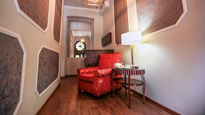 A hallway with a red floral armchair, a small table with a lamp, and a decorative wall panel. - Tea for Two Hotel (Tbilisi)
