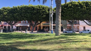 A sunny urban street with palm trees, a café, and parked cars. - APT.1ST LINE BEACH. AT STREET LEVEL. 2 BEDROOMS/4 PERSONS. WIFI AND NETFLIX.  (Málaga)