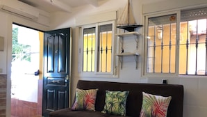 A living room with a dark brown sofa, three tropical patterned cushions, a hanging light fixture, and a door leading outside. - APT.1ST LINE BEACH. AT STREET LEVEL. 2 BEDROOMS/4 PERSONS. WIFI AND NETFLIX.  (Málaga)