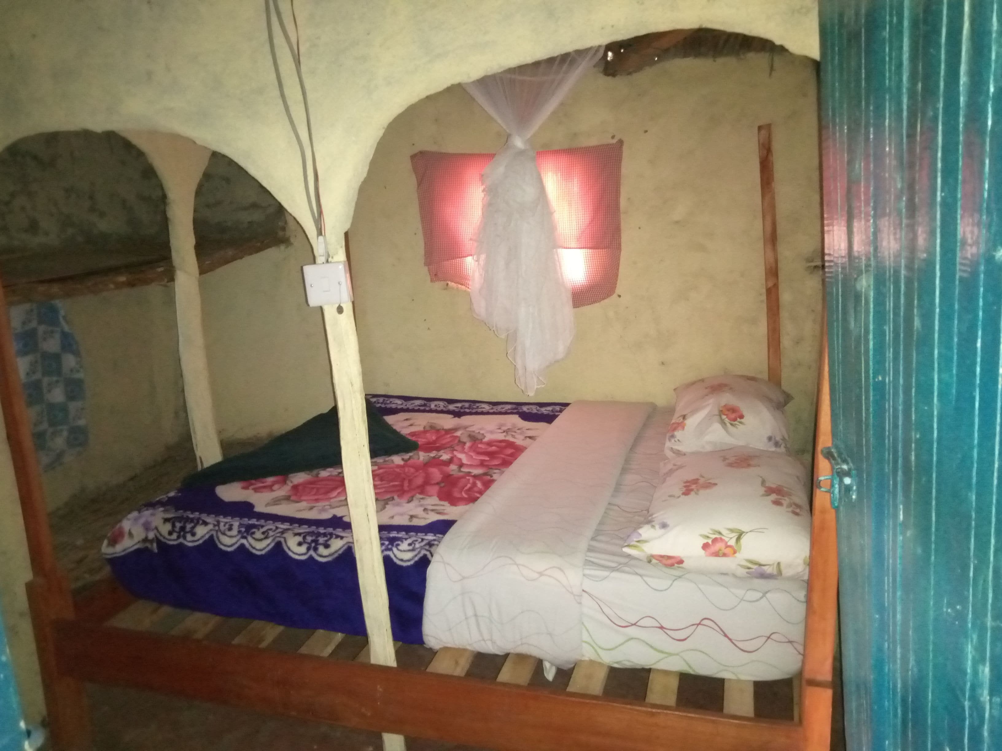 A single bed with a floral bedspread, a mosquito net, and a wall-mounted light fixture.