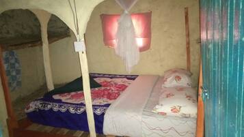 A single bed with a floral bedspread, a mosquito net, and a wall-mounted light fixture.