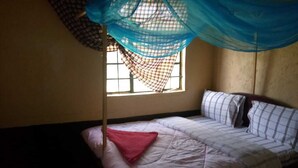 A single bed with a mosquito net, a window with bars, and a plain wall. - Leruk Guest House (Maasai Mara)