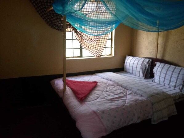 Uma cama de solteiro com mosquiteiro, janela com grades e parede simples.
