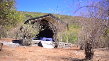 Una estructura tipo tienda de campaña sobre una base de piedra, rodeada de vegetación escasa y un cielo despejado.