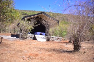 Una estructura tipo tienda de campaña sobre una base de piedra, rodeada de vegetación escasa y un cielo despejado.