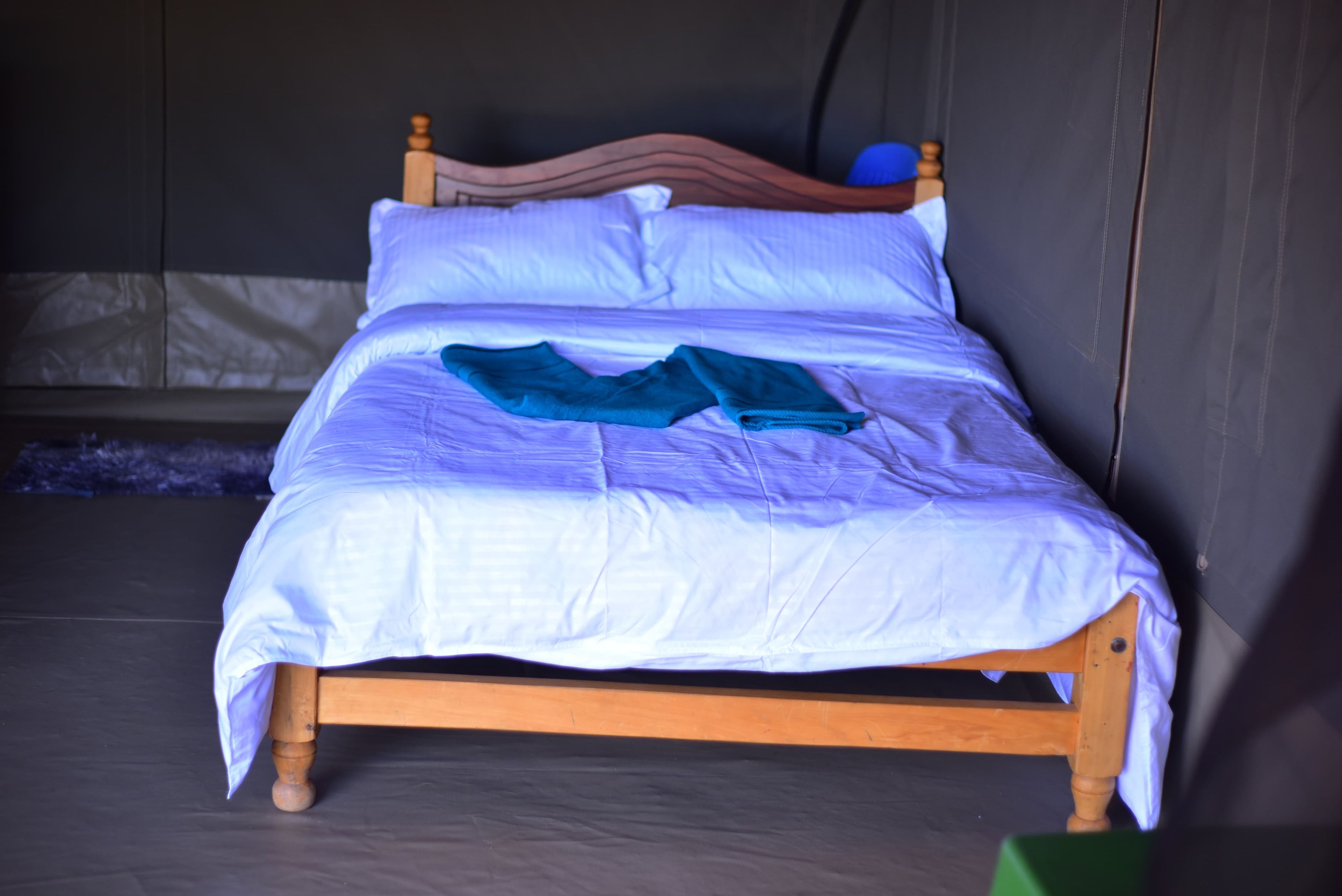 Una cama individual con estructura de madera, ropa de cama blanca y una prenda azul sobre ella.