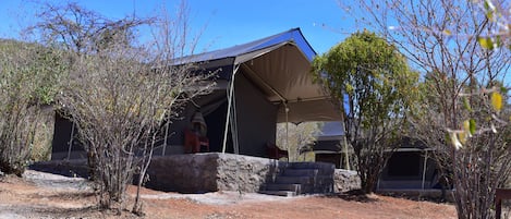 Una estructura cubierta con base de piedra, rodeada de vegetación escasa y un cielo despejado.