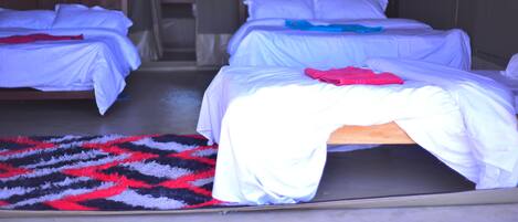 Una habitación con dos camas, cada una con ropa blanca y una manta azul. Hay una alfombra estampada en el suelo.