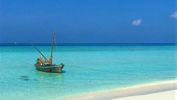 Un barco fondeado en un mar turquesa transparente, con una playa de arena blanca al frente.