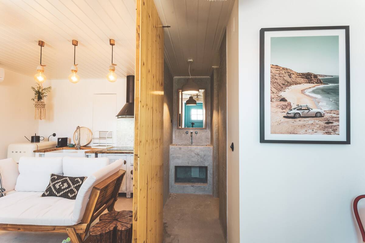 A modern kitchen with a wooden accent wall, a framed beach photograph, and pendant lighting.