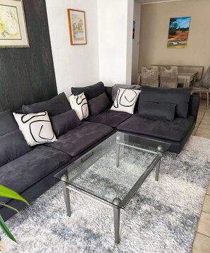 A modern living room with a sectional sofa, a glass coffee table, and a fluffy rug.