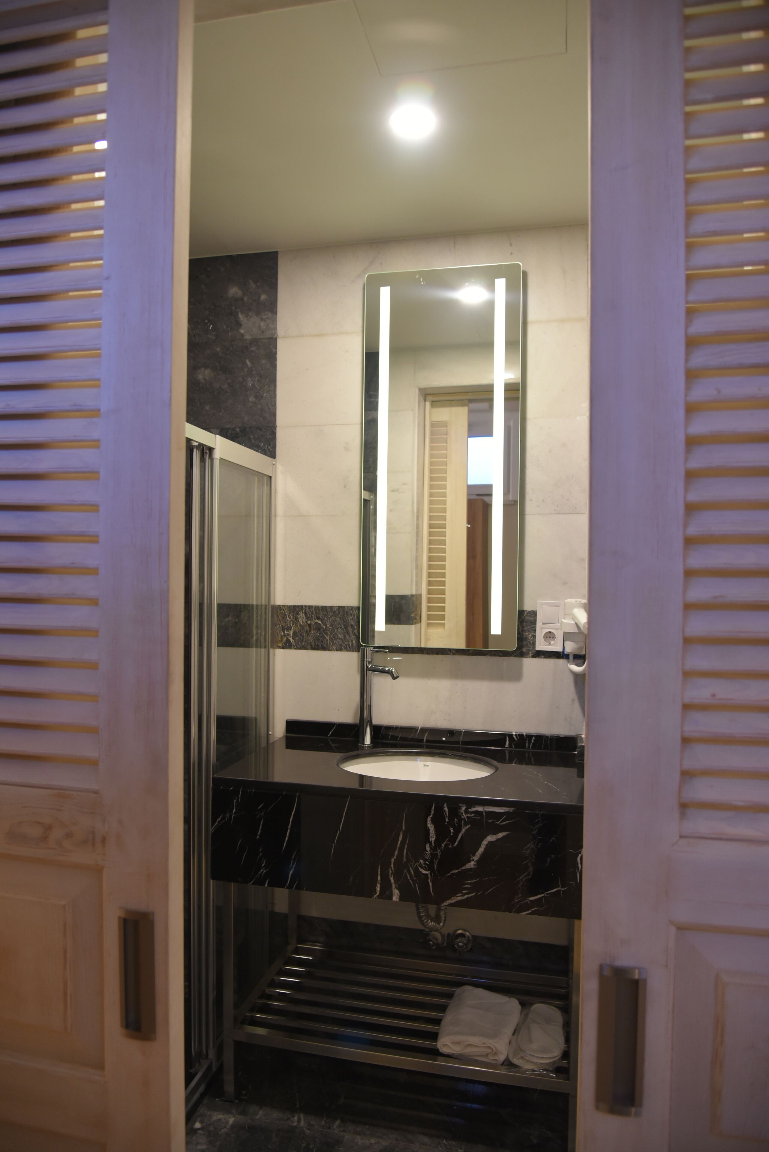 A bathroom with a glass shower enclosure, a white sink, and a marble countertop.