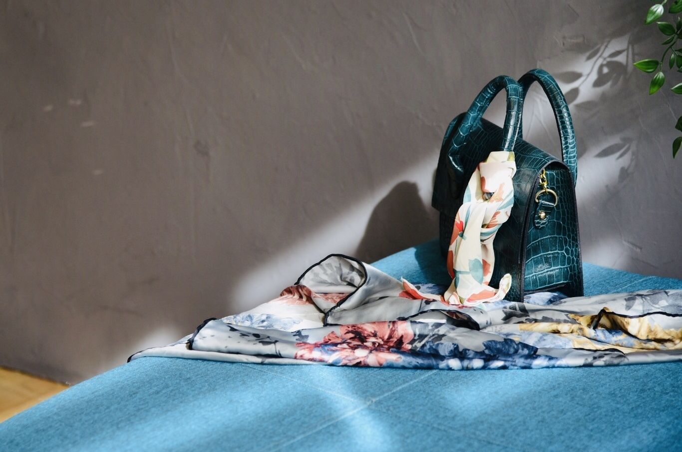 A bed with a blue blanket and a green handbag on it.