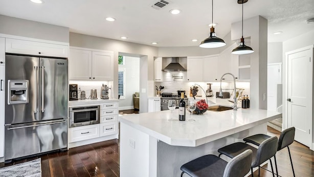 A modern kitchen with stainless steel appliances, white cabinetry, and a central island with bar stools.