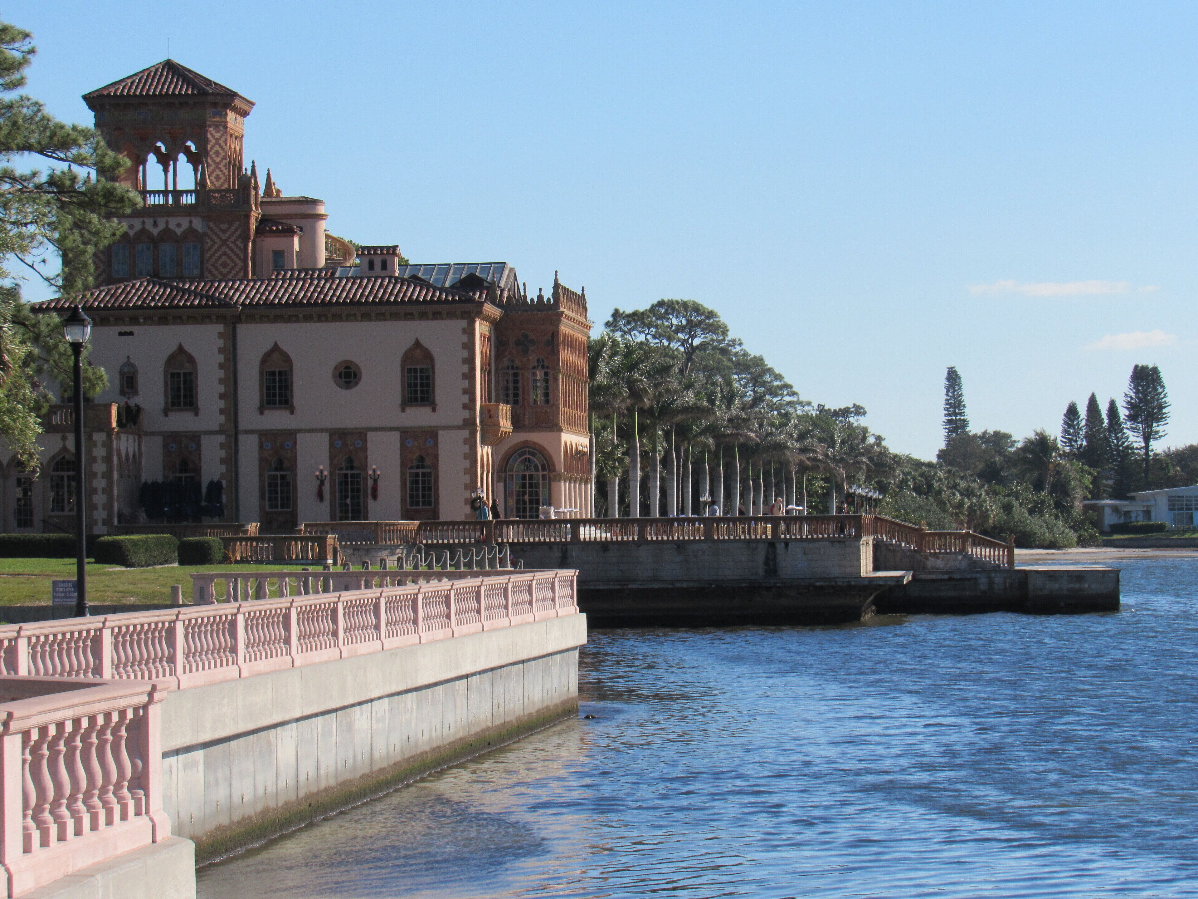 A large, historic building with a tower and multiple windows, situated next to a body of water.