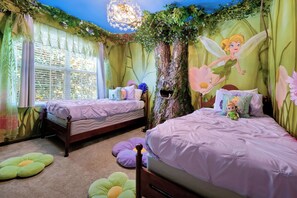 Un dormitorio con dos camas, una ventana y un mural con tema de hadas.
