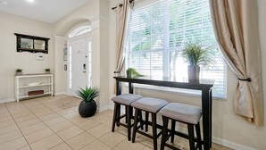 A hallway with a white door, a console table with plants, and a window with curtains. - 6 bed South Facing Pool/Spa Home Free Heat, Disney (Kissimmee)