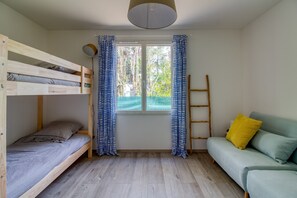 Una habitación con una litera, un sofá, una ventana con cortinas, una escalera y una lámpara.