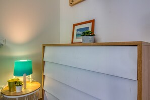 Una habitación con un aparador de madera, una lámpara azul verdosa, una planta pequeña en maceta y un cuadro en la pared.