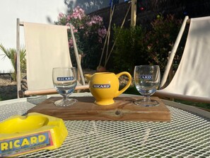 A table with a yellow teapot and two glasses of water, a yellow box labeled "RICARD," and two white chairs. - La Maison, ★ L'her beau d'hier 3-bedroom house (sleeps 8) 300m from the beach ★ (L'Épine)