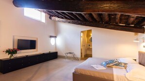 A bedroom with a bed, a TV, a dresser, and a small table with a lamp. - Palazzo Cavarretta (Palermo)