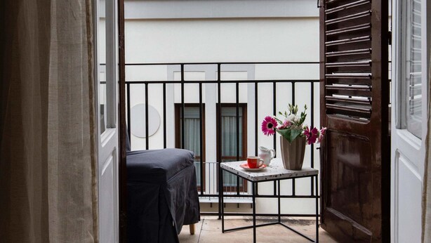 A balcony with a table, a chair, and a vase of flowers. - Palazzo Cavarretta (Palermo)