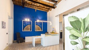 A reception area with a blue wall, a white desk, and a large potted plant. - Palazzo Cavarretta (Palermo)
