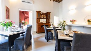A dining area with a wooden table and chairs, a built-in cabinet with glass doors, and a wall-mounted shelf with flowers. - Palazzo Cavarretta (Palermo)