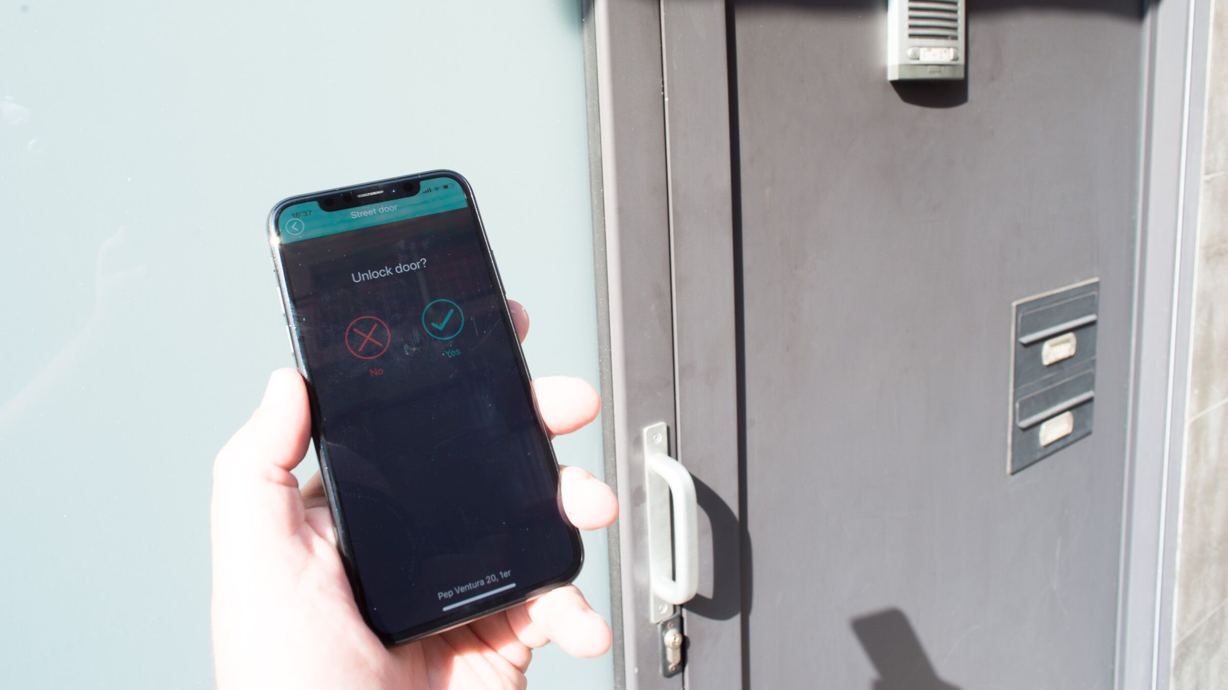 A hand holding a smartphone with a lock screen displaying a 'Street door' and a 'Yes' option for 'Unlock door?'.
