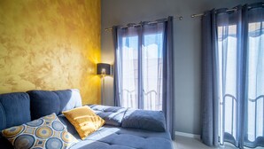 Un salon moderne avec un canapé, des coussins à motifs, une lampe et de grandes fenêtres avec des rideaux.