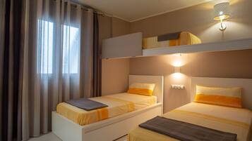 A hotel room with two beds, a bunk bed, a window with curtains, and a wall-mounted light fixture.