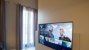 Un salon avec un téléviseur à écran plat fixé au mur, des rideaux et un canapé.