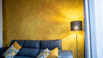 A room with a blue sofa, two patterned pillows, and a floor lamp against a yellow wall.
