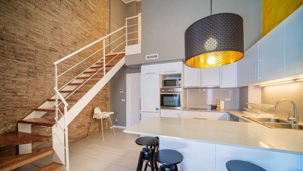 Une cuisine moderne dotée d’un îlot central, de meubles blancs et d’un escalier avec des marches en bois et des rampes blanches.