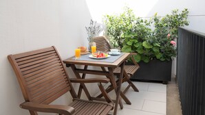 Une table et des chaises en bois sont disposées sur un balcon, accompagnées d’une plante en pot et d’un pot de fleurs.