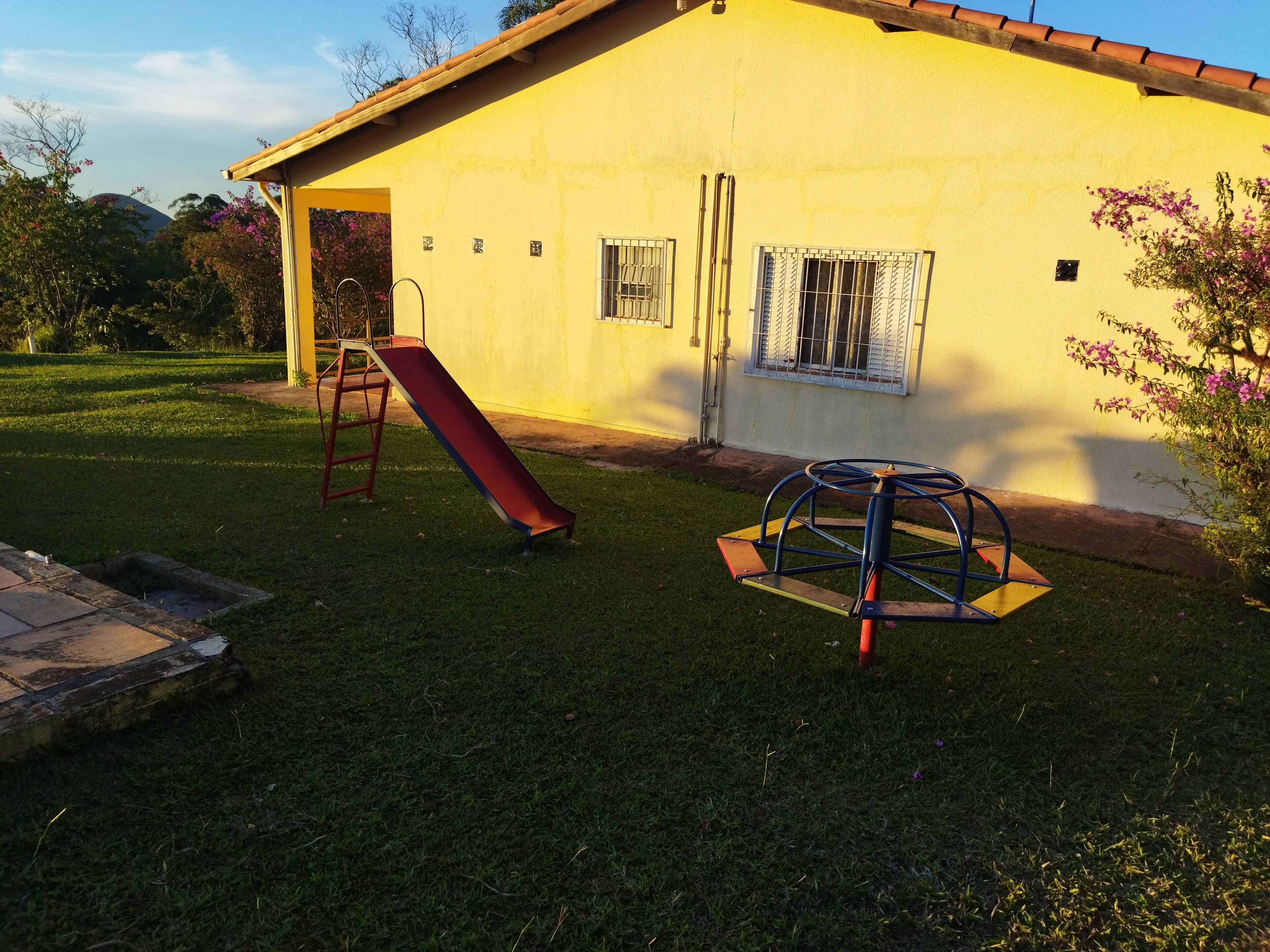 A yellow building with a red slide and a blue swing set in the yard.